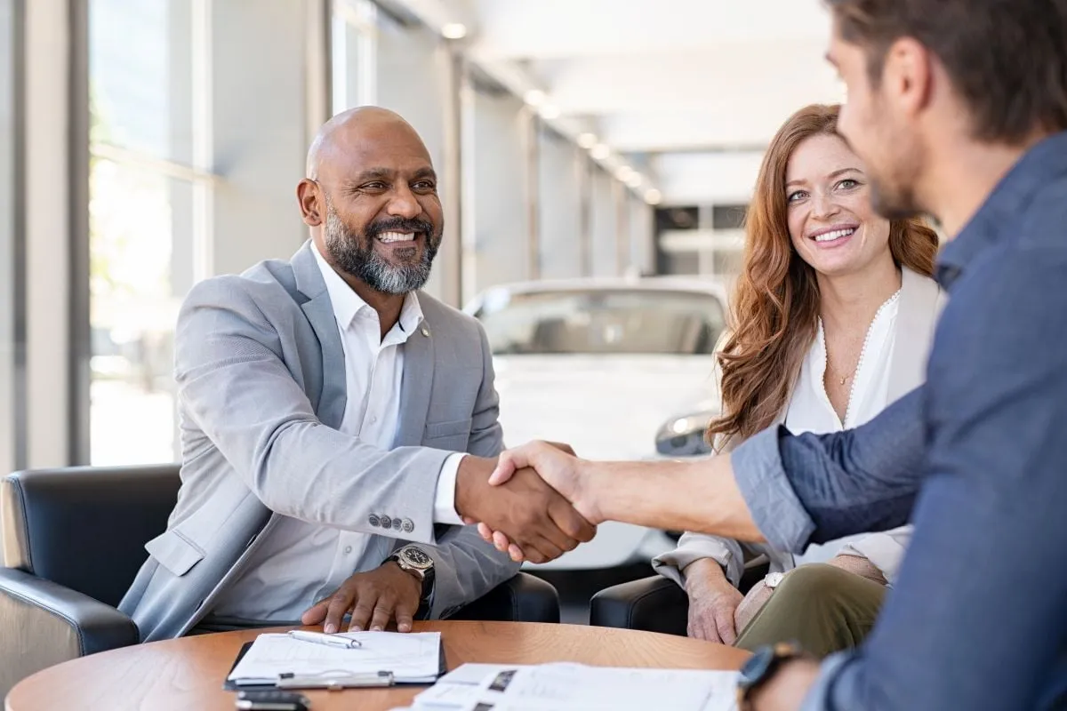A salesperson shaking hands with customers at a dealership